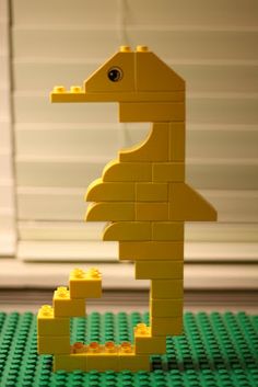 a lego model of a giraffe made out of small yellow bricks, sitting on top of a green mat