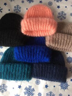 four knitted hats laying on top of a bed covered in snowflakes