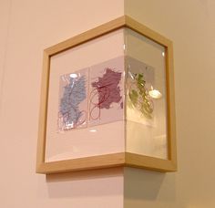 a wooden frame hanging on the wall above a vase with flowers in it and another piece of artwork behind it