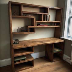 a wooden desk sitting in front of a window next to a book shelf with books on it