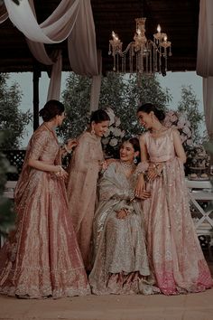 three women in dresses standing next to each other near a chandelier and flowers