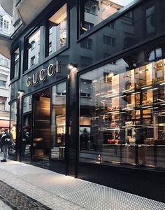 people are walking down the sidewalk in front of a gucci store on a city street