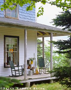 a porch with rocking chairs on it next to a tree and house in the background