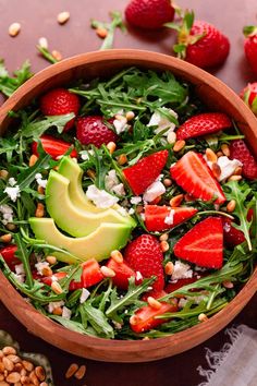 a salad with strawberries and avocado in a wooden bowl on a table