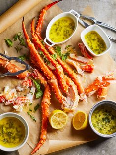 lobsters and other seafood on a cutting board with dipping sauces, lemon wedges and parsley