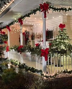 a house decorated for christmas with red bows and lights on the front porch, covered in greenery