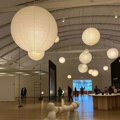 people are standing in an open space with white lanterns hanging from the ceiling and round lights above them