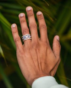 a person's hand with two wedding bands on top of their fingers and palm leaves in the background