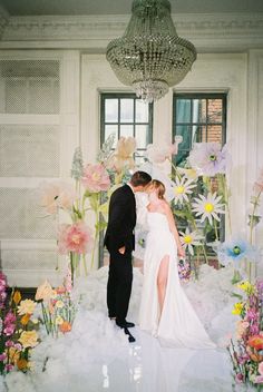 a bride and groom are kissing in front of an arrangement of flowers on the floor