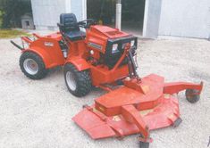 a red lawn mower parked in front of a building with a garage behind it