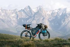 a bicycle parked on top of a grass covered hill with mountains in the back ground