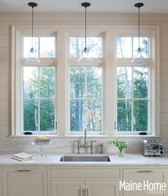 a kitchen with three windows and white cabinets