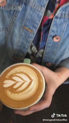 a person holding a cup of coffee with an artistic design on the foam in their hand