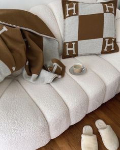 a white couch with two pillows and slippers on it next to a cup of coffee