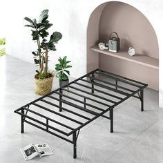 a metal bed frame next to a potted plant and magazine rack on the floor