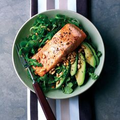 a plate with salmon, avocado, and spinach on it next to a fork