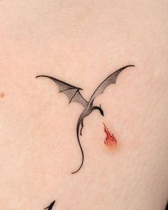 a small tattoo on the back of a woman's left shoulder with a dragon flying over it