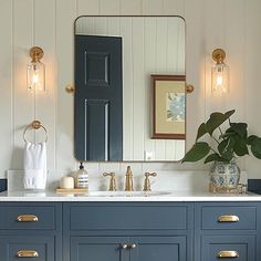 a bathroom with blue cabinets and gold pulls on the doors, mirrors and lights above the sink