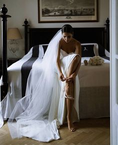 a woman in a wedding dress sitting on a bed with her veil over her head