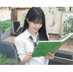 a young woman is reading a book in front of potted plants and other items