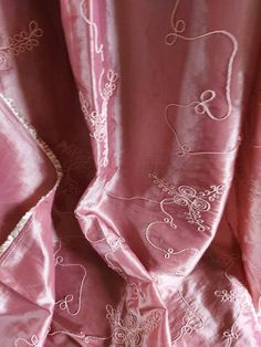 a pink curtain with white embroidered designs on it