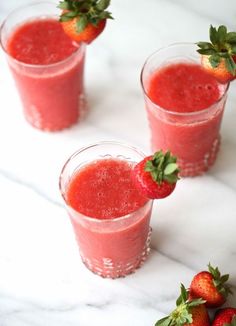 three glasses filled with strawberry juice on top of a white marble table next to strawberries