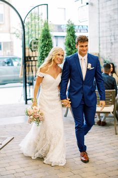 a bride and groom are walking down the street holding hands in front of some people