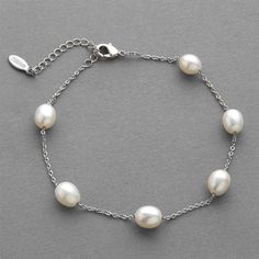 a bracelet with white pearls on a silver chain and a small charm is attached to the clasp