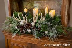 candles are lit on top of a mantel decorated with greenery and pine cones