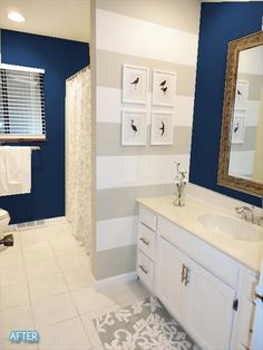 a bathroom with blue and white striped walls, tile flooring and a large mirror on the wall