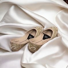 a pair of gold shoes sitting on top of a white satin covered bed sheet,