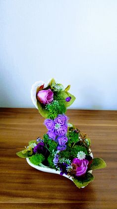 purple flowers are arranged in a white vase on a wooden table with green leaves and greenery