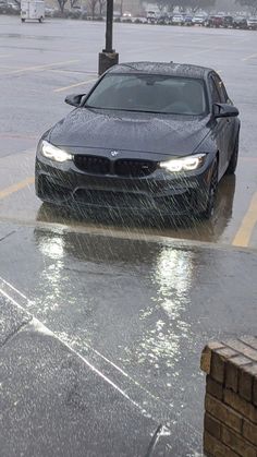 a black car driving through a parking lot in the rain