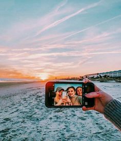 a person holding up a cell phone to take a photo on the beach at sunset