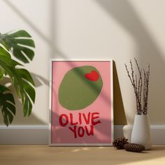 a poster with the words olive you on it next to a potted plant and pine cone