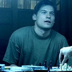 a man is playing chess in front of another man who has his hand on the board