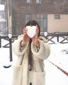 a woman holding up a heart shaped snowball in front of her face while standing outside