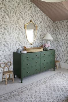 a green dresser and mirror in a room with wallpapered walls, rugs and chairs