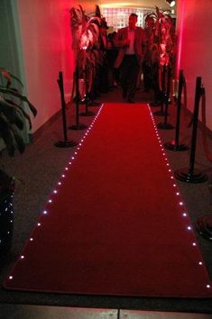 a red carpet with white lights on it and people walking down the hallway in the background