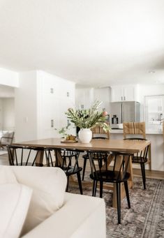 a dining room table with chairs and a vase filled with flowers on top of it