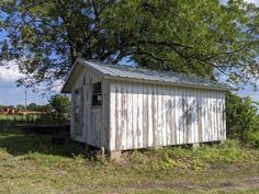 an old outhouse sits in the middle of a grassy field next to a tree