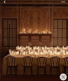 a long table with many lit candles on it and chairs in front of the table