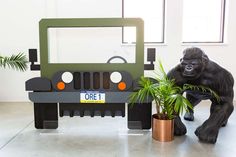 a gorilla statue standing next to a fake jeep with a plant in front of it