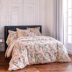 a bed with floral comforter and pillows in a white room next to a window