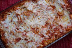 a square casserole dish with cheese and tomato sauce in it on a red cloth