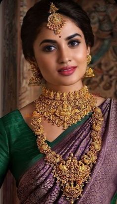 a woman in a green and purple saree with gold jewelry on her neck, posing for