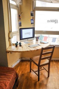 a desk with a computer on top of it in front of a window next to a bed