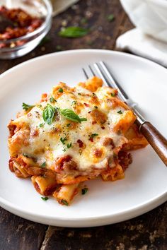 a white plate topped with lasagna covered in sauce and cheese next to a fork