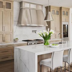 a kitchen with marble counter tops and white chairs in front of an island that has flowers on it