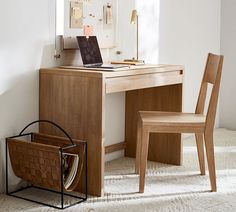 a wooden desk with a laptop computer on top of it next to a basket and chair